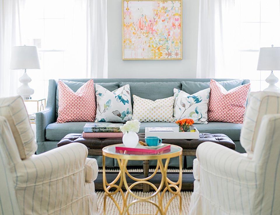 Transitional living room with sage green sofa, pink and teal patterned pillows, brass round table, and soft neutral palette
