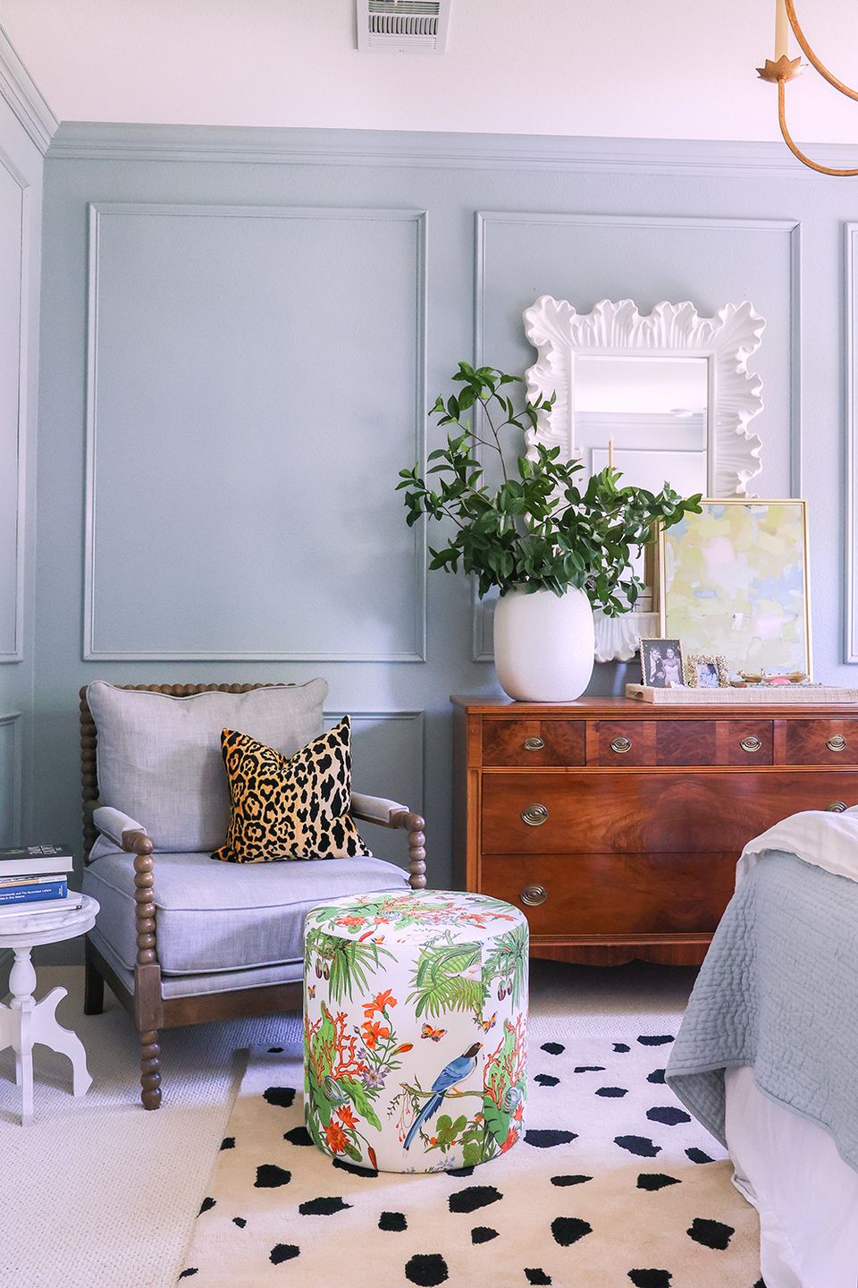 Soft maximalist bedroom with pale blue paneling, tropical pouf, and mixed vintage furnishings