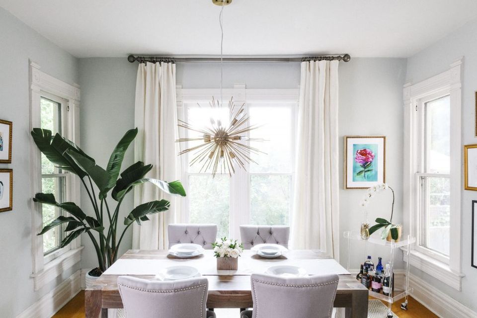 Contemporary dining room with soft sage walls and floor-to-ceiling cream drapery framing botanical view