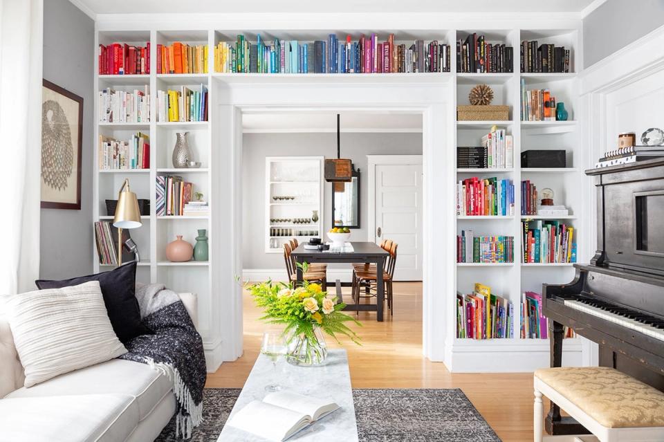 Modern eclectic space with floor-to-ceiling white shelving displaying colorful books, creating a bold focal point in a neutral living area.