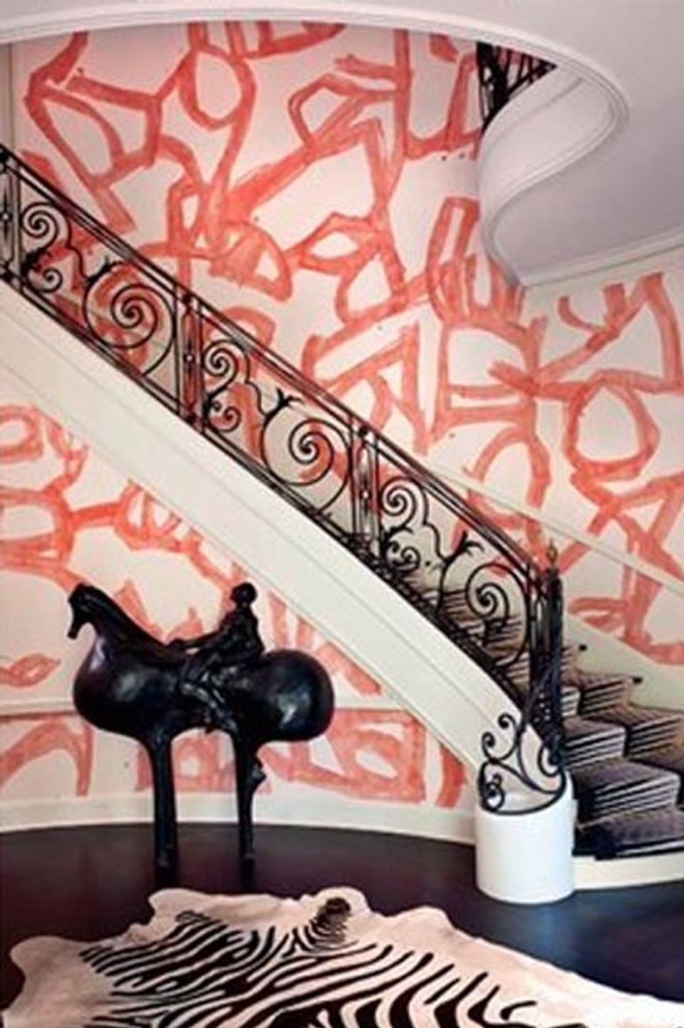 Contemporary curved staircase with bold coral abstract wallpaper, ornate iron railing, and sculptural black accent pieces