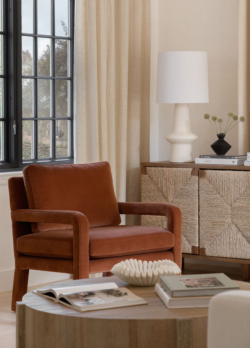 Warm, layered corner with burnt orange velvet chair, textured wood storage, and cream drapes in earthy tones