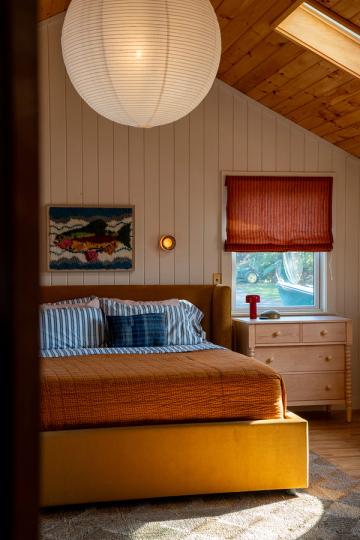 Rustic cabin bedroom with warm wood paneling, mustard bed frame, and blue striped pillows