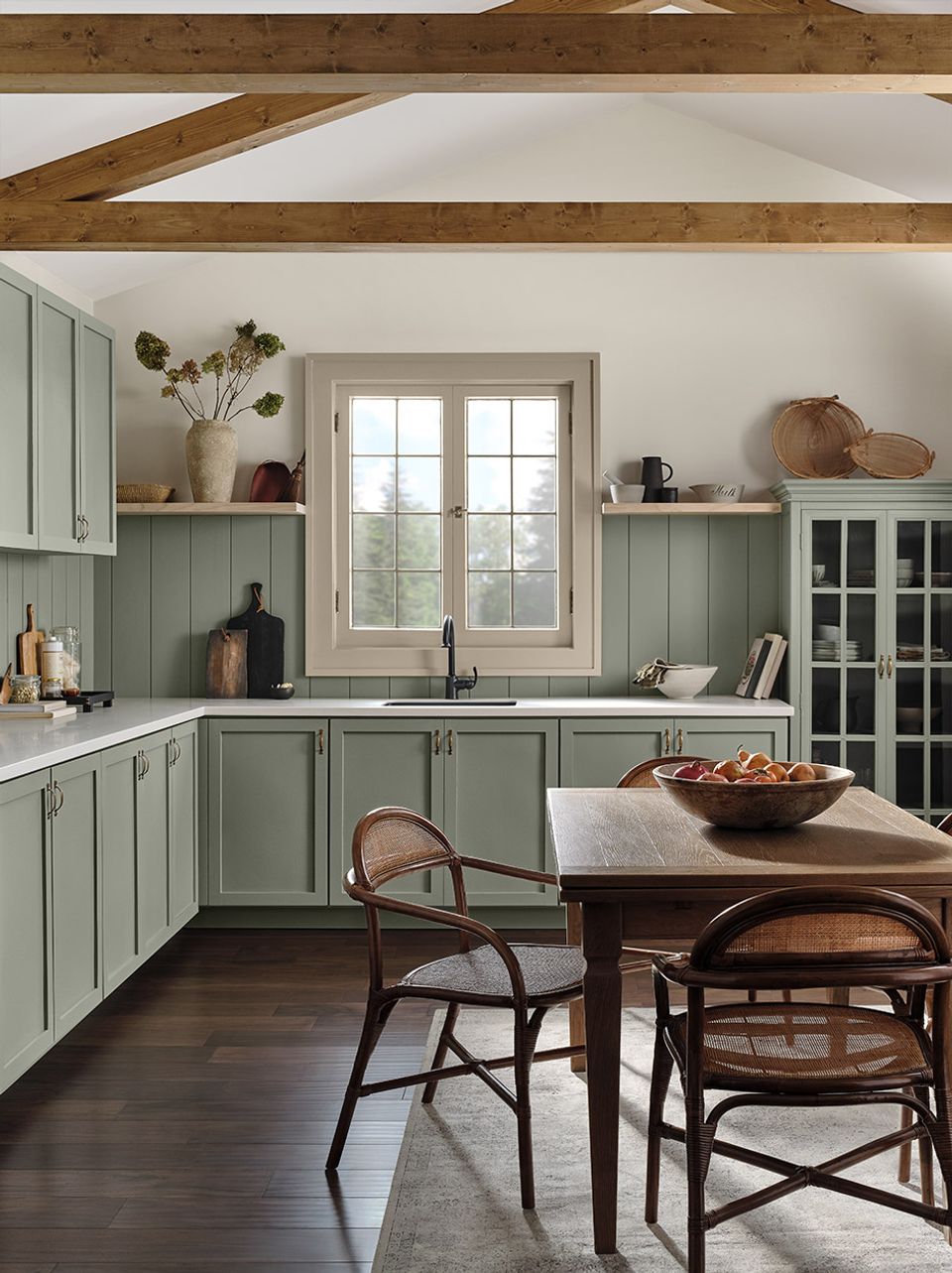 Farmhouse kitchen featuring sage green cabinetry, exposed wood beams, and classic dining setup