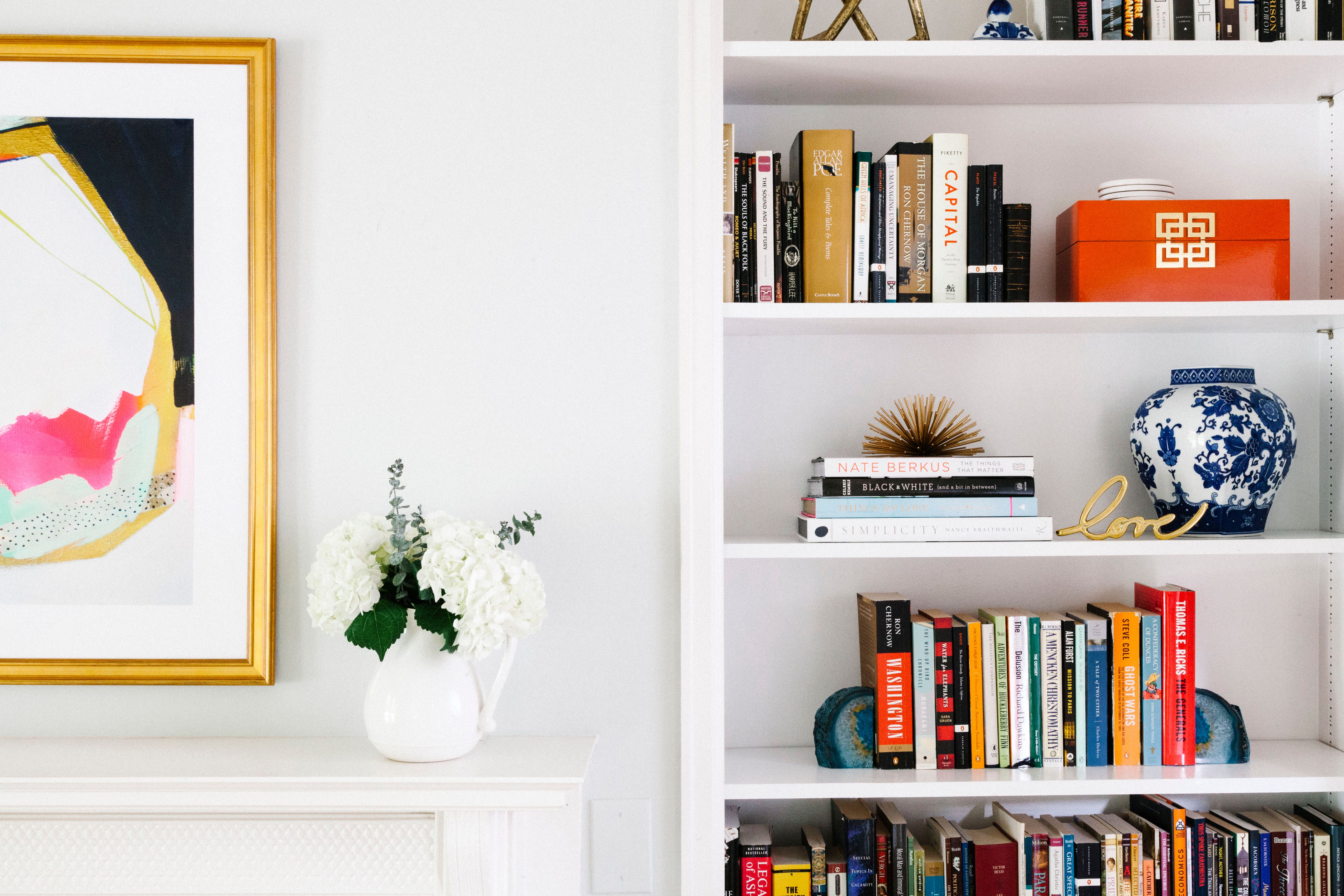 Modern gallery wall with colorful abstract art above open shelving styled with books, ceramics, and greenery in bright, curated aesthetic