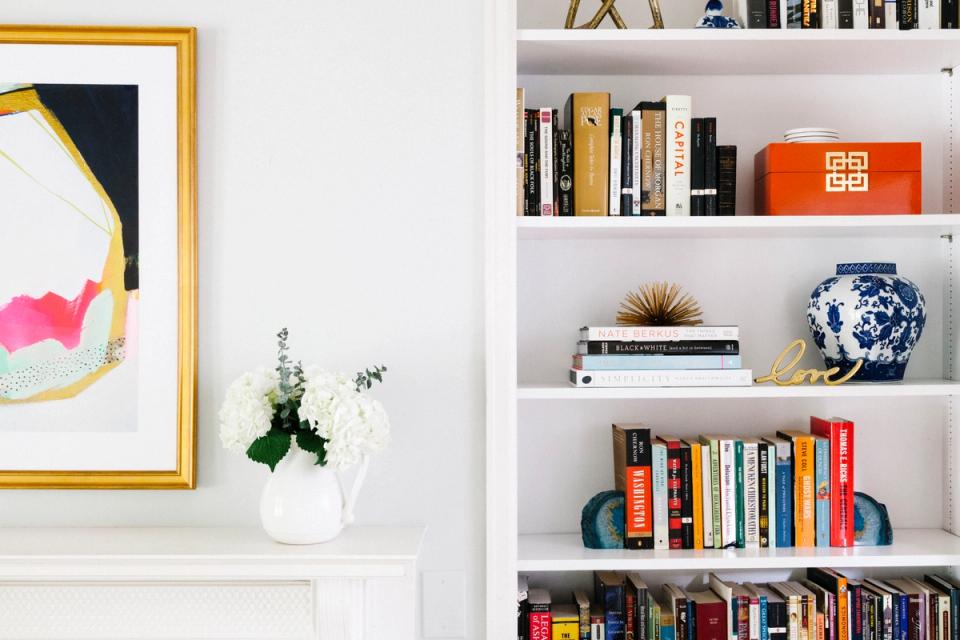 Modern gallery wall with colorful abstract art above open shelving styled with books, ceramics, and greenery in bright, curated aesthetic