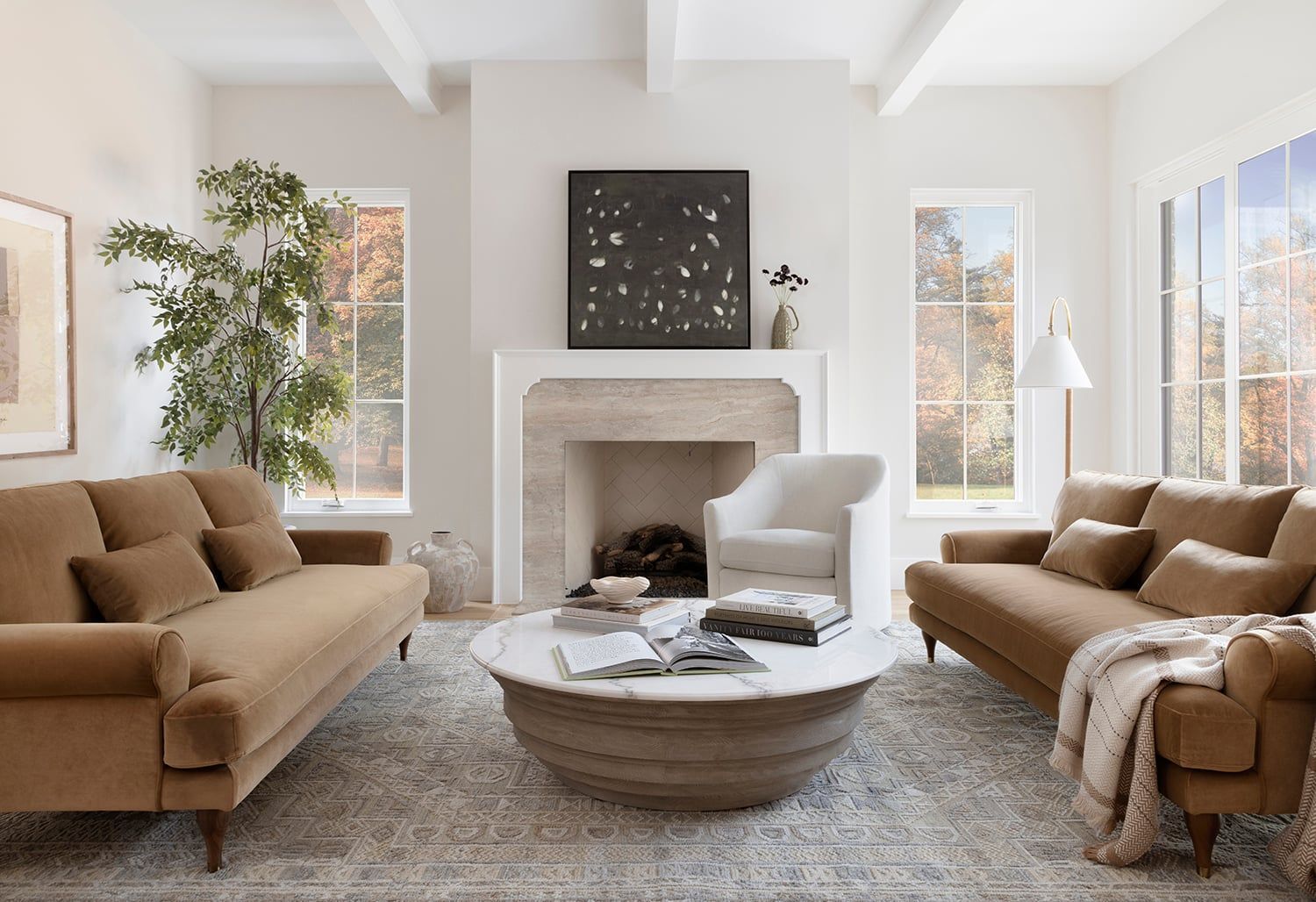 Warm neutral living room with caramel sofas, round wood coffee table, and fireplace mantel in soft contemporary-traditional style