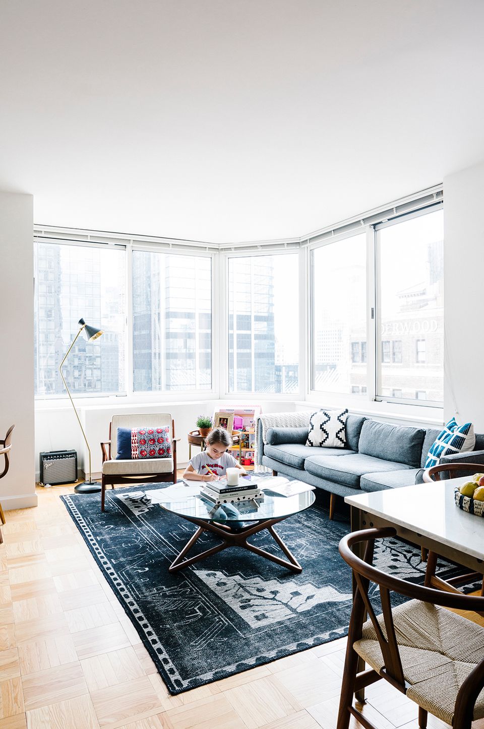 Modern minimalist living room with floor-to-ceiling windows, slate blue sofa, and dark patterned area rug