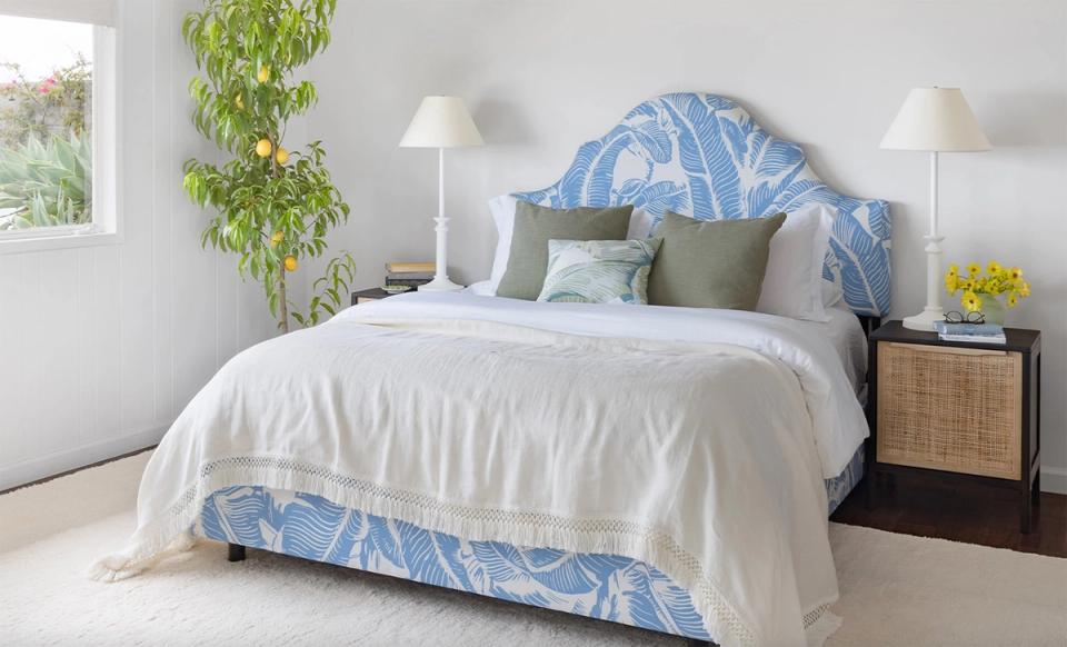 Serene coastal bedroom with blue patterned headboard, white linens, and natural greenery accents