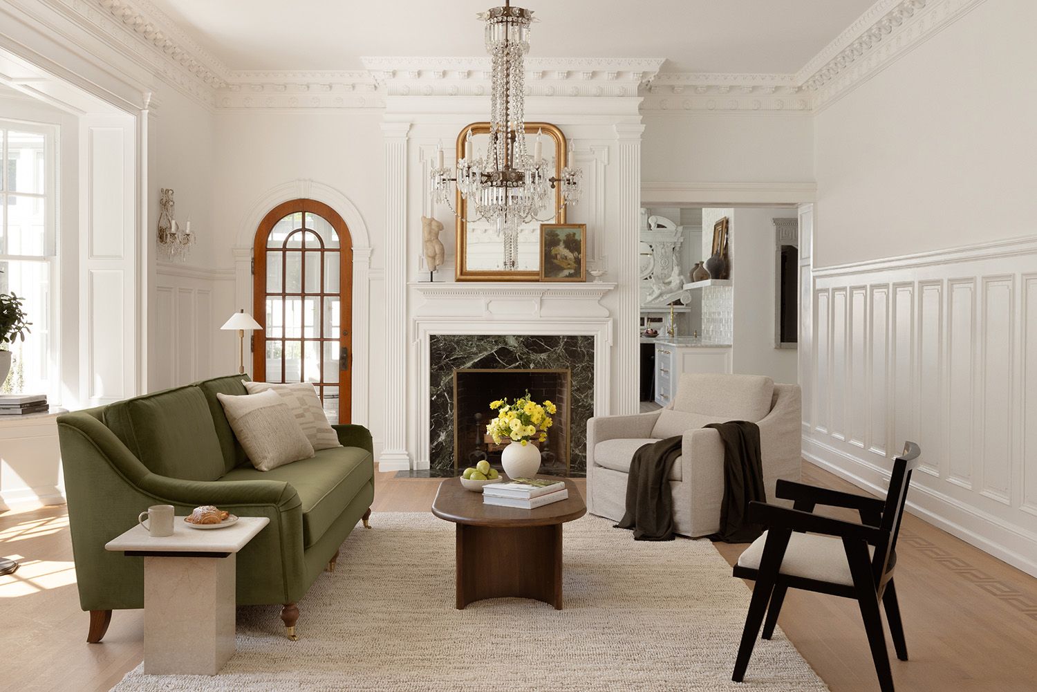 Transitional living room with sage green sofa, cream walls, black accents, and brass chandelier creating a sophisticated, airy mood