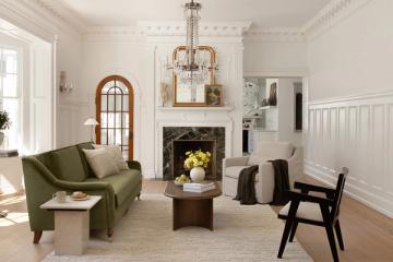 Transitional living room with sage green sofa, cream walls, black accents, and brass chandelier creating a sophisticated, airy mood