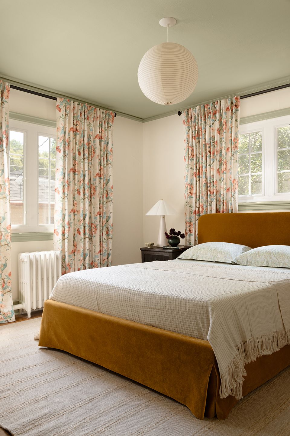 Vintage-inspired bedroom with mustard upholstered bed and floral curtains