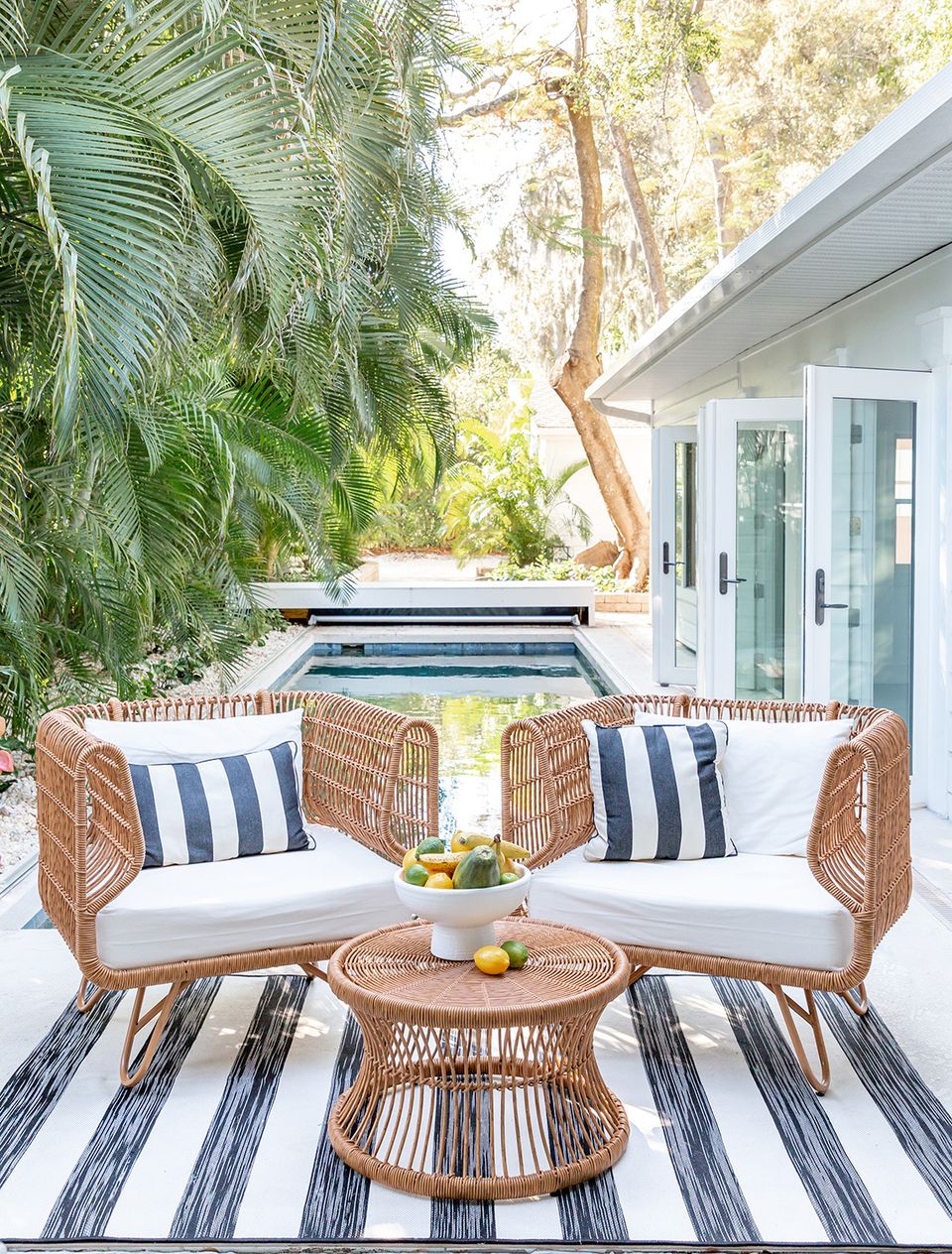 Coastal living space with woven wicker chairs, navy striped pillows, striped rug, and relaxed tropical atmosphere.