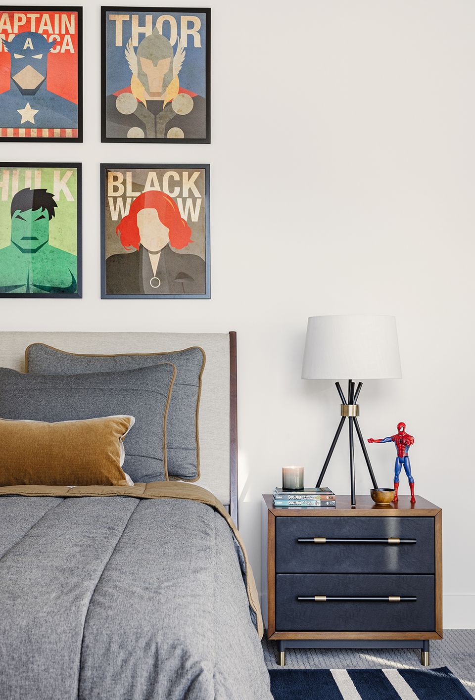 Contemporary bedroom with bold comic-inspired artwork, gray upholstered bed, warm wood nightstand, and minimalist styling balancing superheroes with sophisticated design.