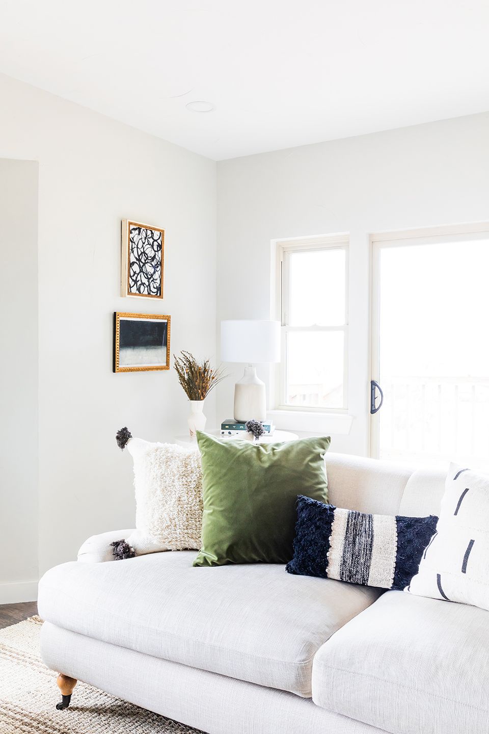 Serene white room with green, navy, and cream textured throw pillows on modern sofa