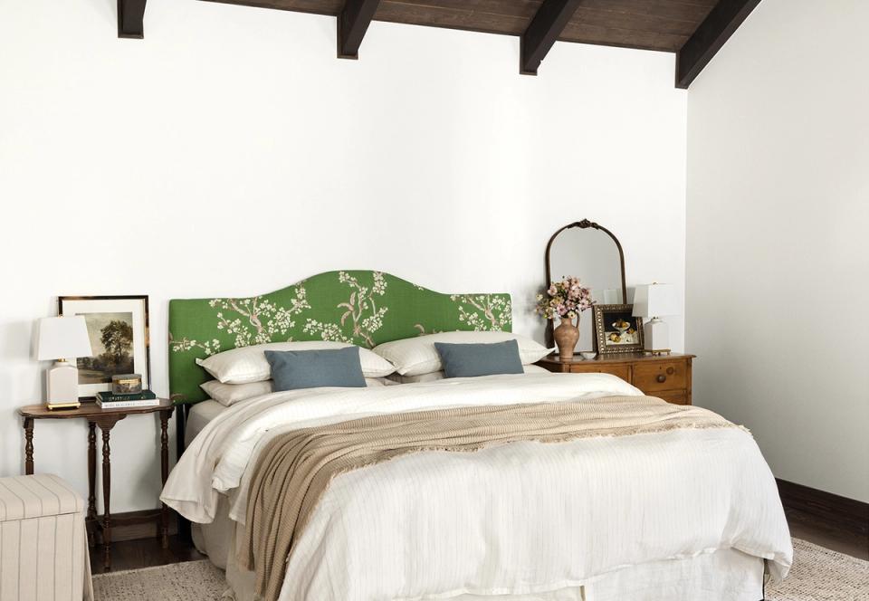 Cottage-style bedroom featuring a striking green arched headboard against white walls with warm wood accents and vintage charm