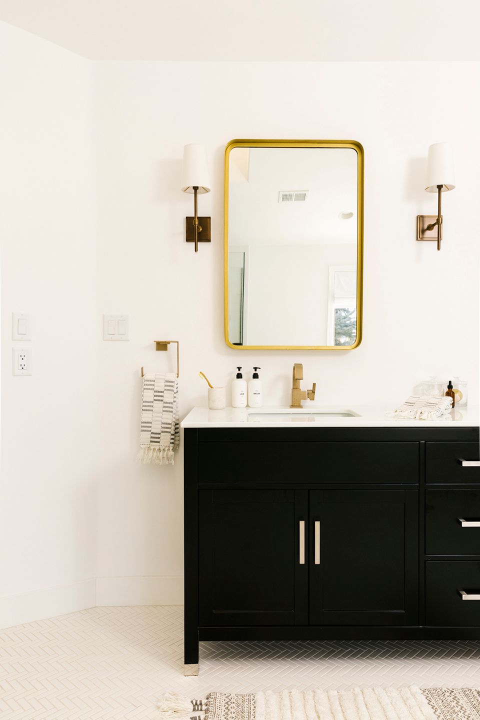 Minimalist bathroom with black vanity, brass-framed mirror, and sculptural wall sconces
