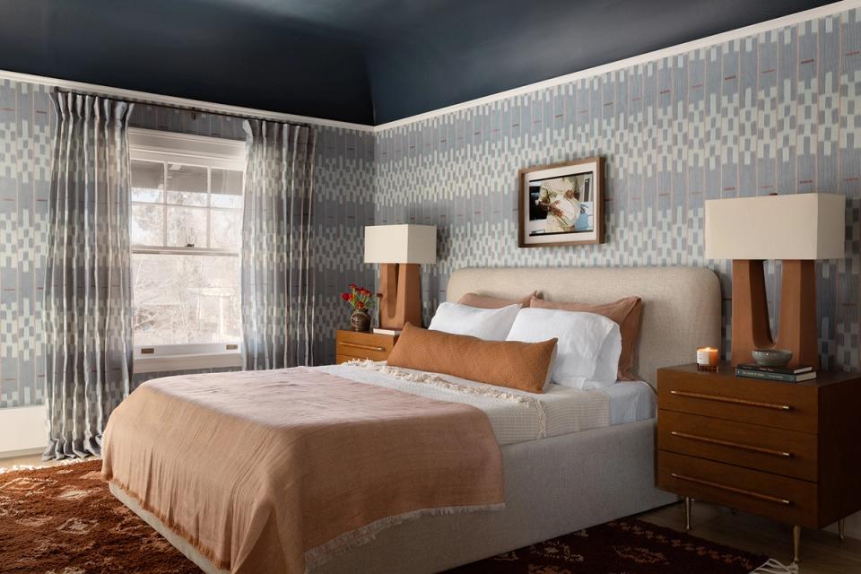 Contemporary bedroom with geometric patterned wallpaper, navy ceiling, warm wood nightstands, and crisp white bedding.