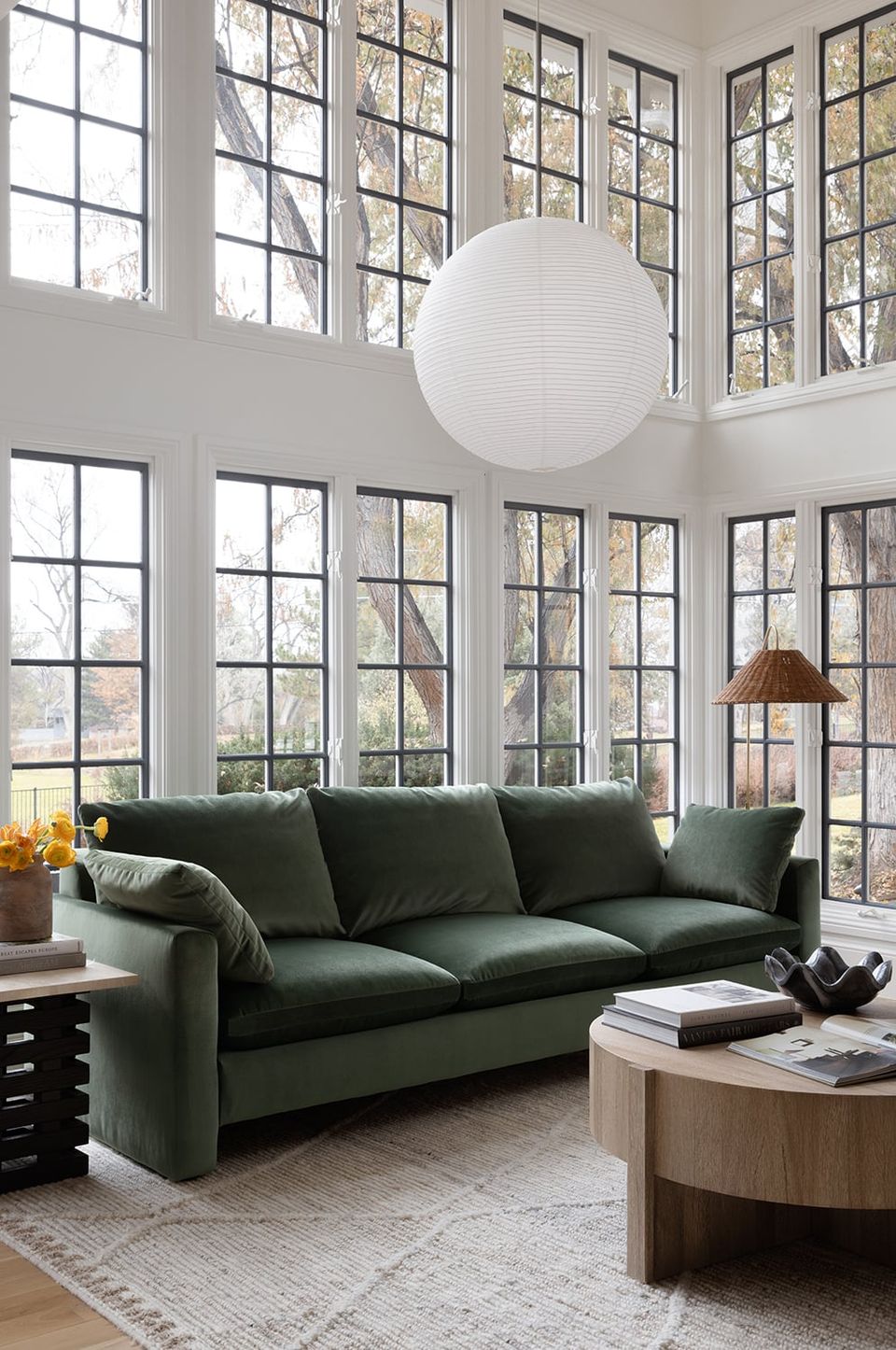Modern transitional living room featuring forest green sofa, expansive window walls, and organic pendant fixture