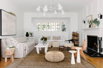 Coastal cottage living room with curved cream sofa, woven poufs, and soft nautical accents in calm, understated palette.