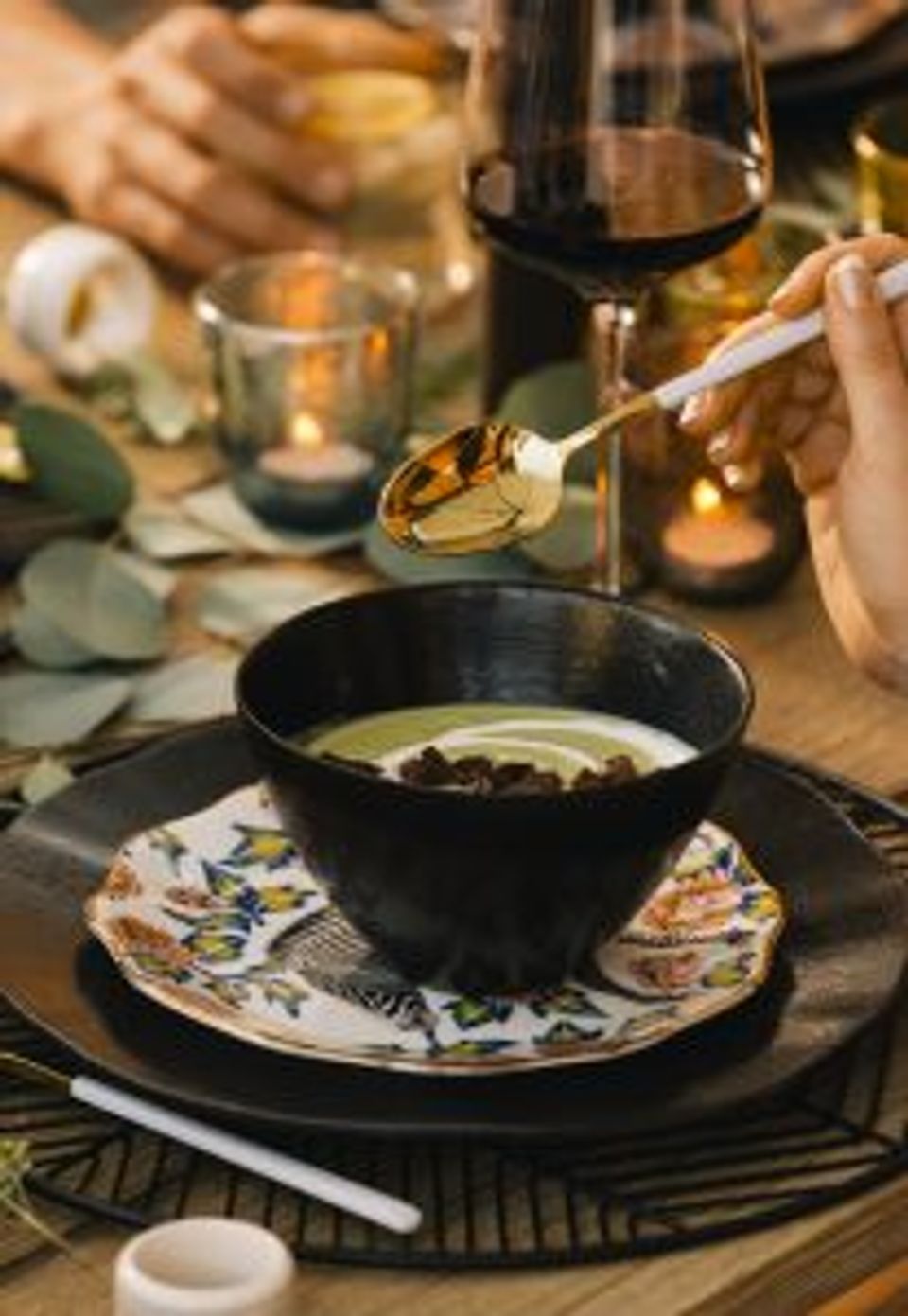 Elegant evening tablescape with black bowls, patterned plates, wine, and candlelit ambiance