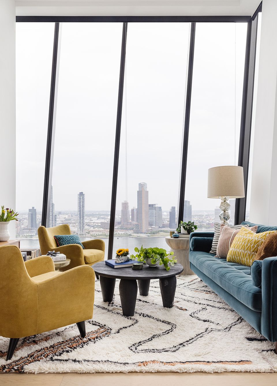 Urban high-rise living room with vibrant mustard and teal seating, city skyline views, geometric rug, and modern color contrast.