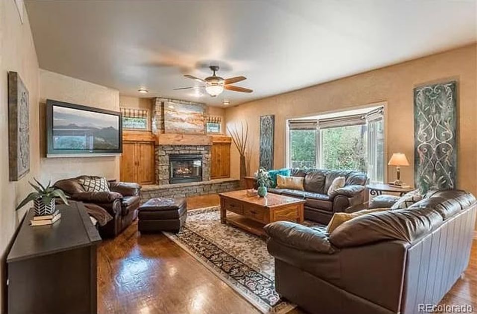 Warm traditional living room with golden-tan walls, dark leather seating, fireplace focal point, and rich wood accents
