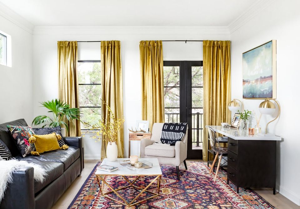 Bright living room with gold curtains, jewel-toned Persian rug, and mustard accent pillows creating vibrant color pops against neutral walls.