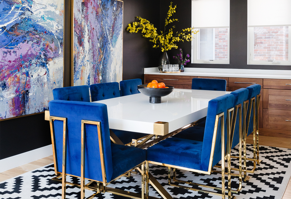 Modern dining space with bold cobalt blue banquette seating, white table, and gold accents against dramatic black accent wall with abstract art.