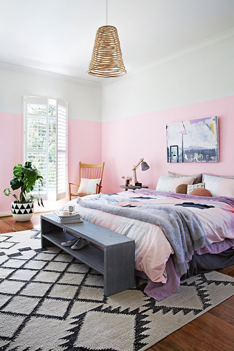 Contemporary bedroom blending soft pink and white tones with rattan pendant, patterned rug, and casual elegance.