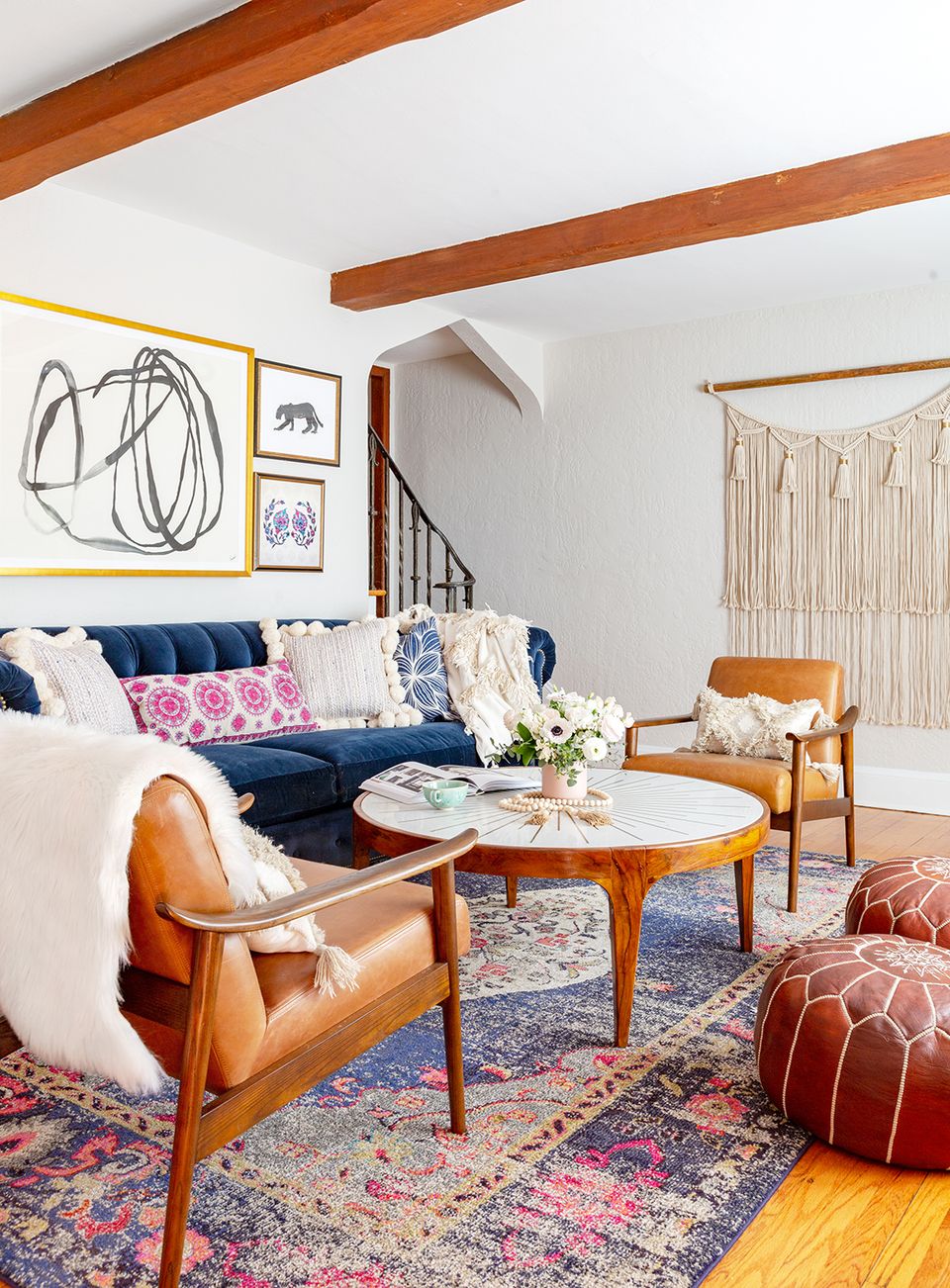 Eclectic boho space combining navy sofa, cognac leather chair, vibrant patterned rug, and wood beam details