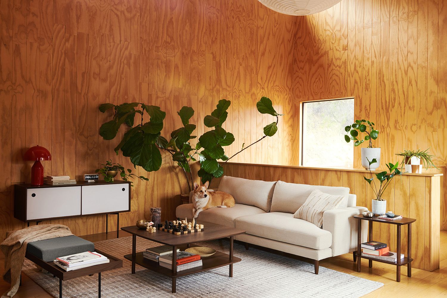 Warm mid-century modern living room with wood paneling, cream sofa, and lush plant styling
