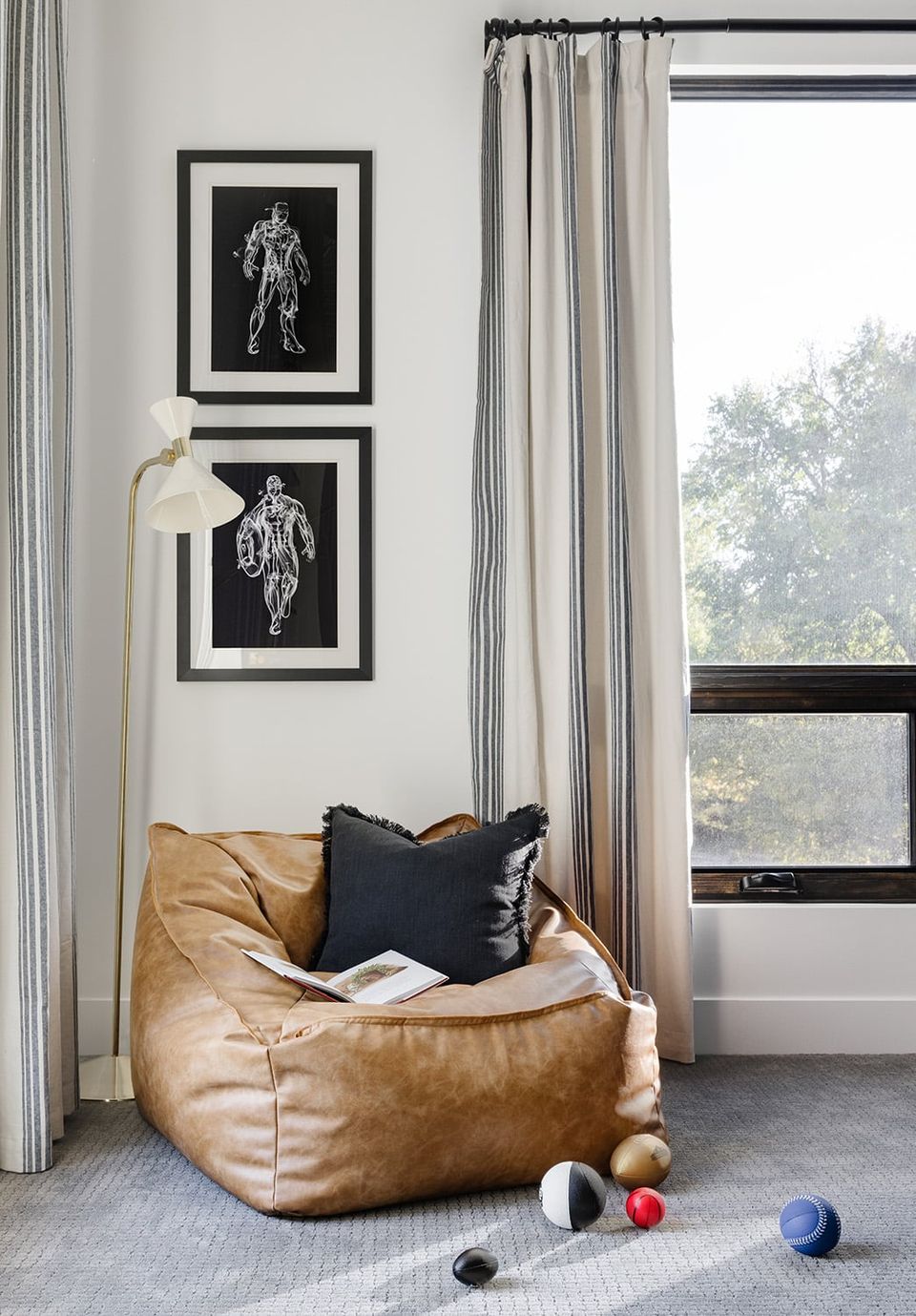 Sophisticated reading nook with minimalist black and white artwork, caramel leather bean bag, and neutral striped curtains creating a calm, modern aesthetic