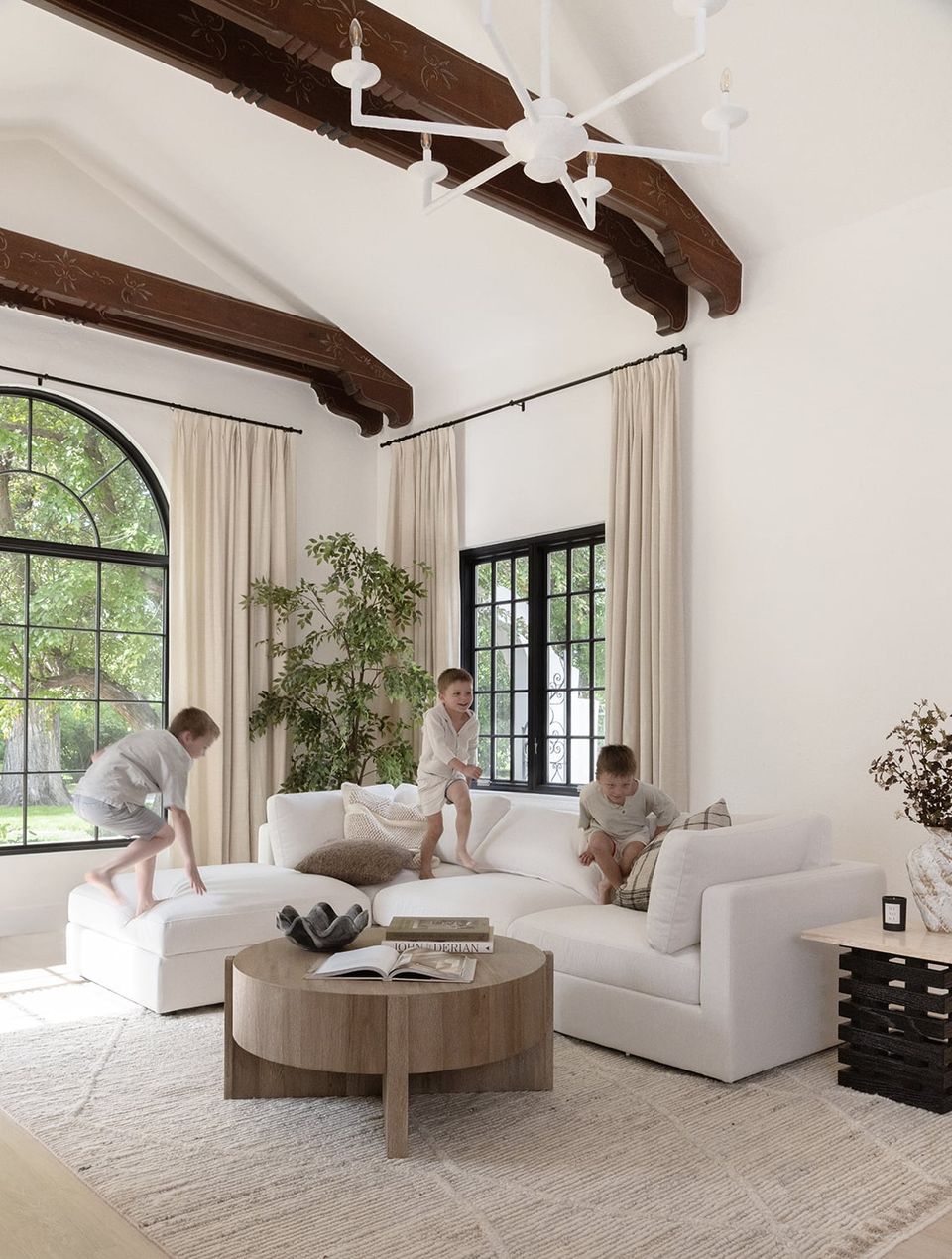 Bright modern farmhouse living room with white sectional, dark wood beams, and natural light from oversized windows