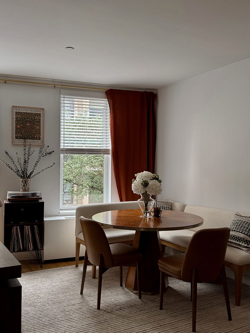 Bright dining nook with round wood table, mid-century chairs, burgundy curtains, and natural light