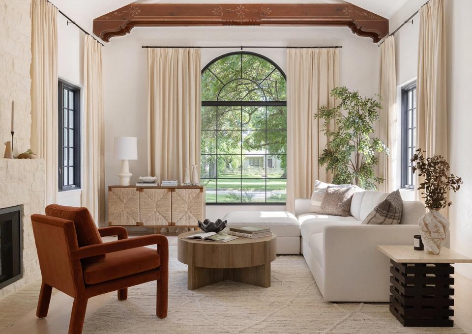 Sophisticated living room with burnt orange chair, cream sofa, and arched window framed by linen curtains
