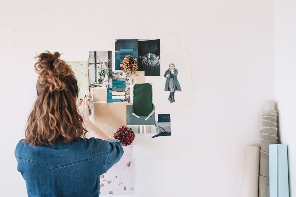 Curated gallery wall with mixed-media artwork, photographs, and fabric swatches in teal, navy, and natural tones creating a modern mood board aesthetic.