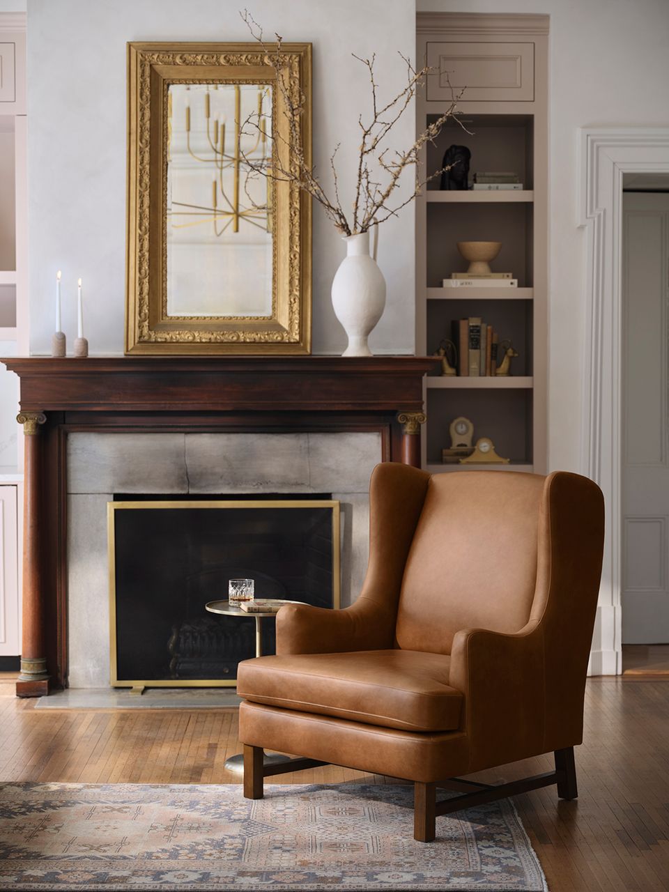 Classic living room with cognac leather chair, dark wood fireplace, gold mirror, and curated shelving