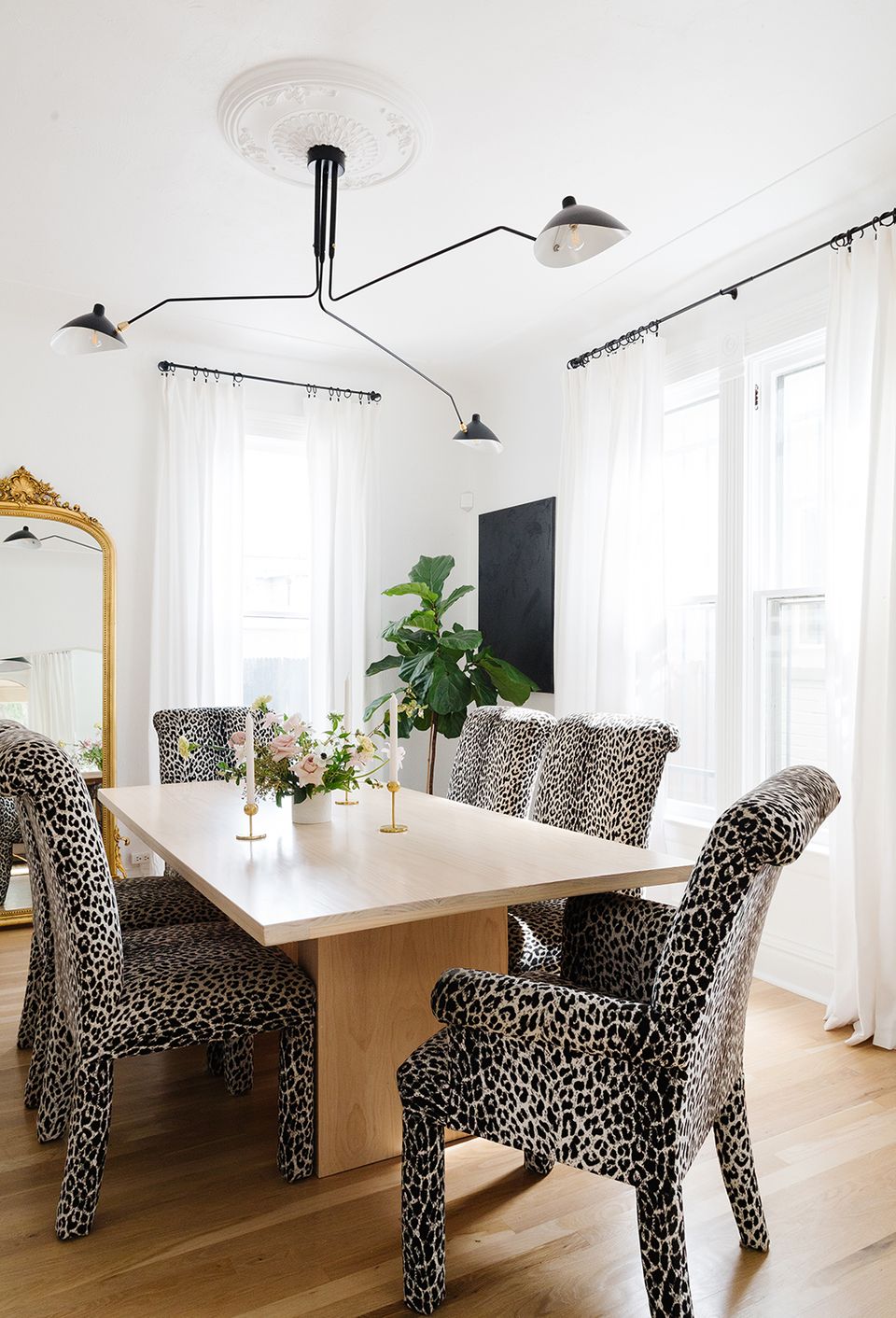 Modern dining room with leopard-print chairs, sculptural black pendant lights, and minimalist white table.