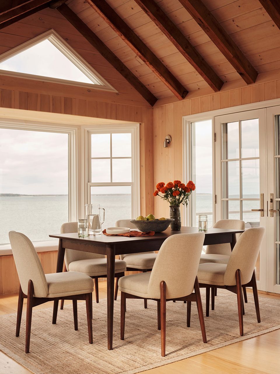 Warm wood dining space with vaulted ceiling, cream upholstered chairs, and waterfront views