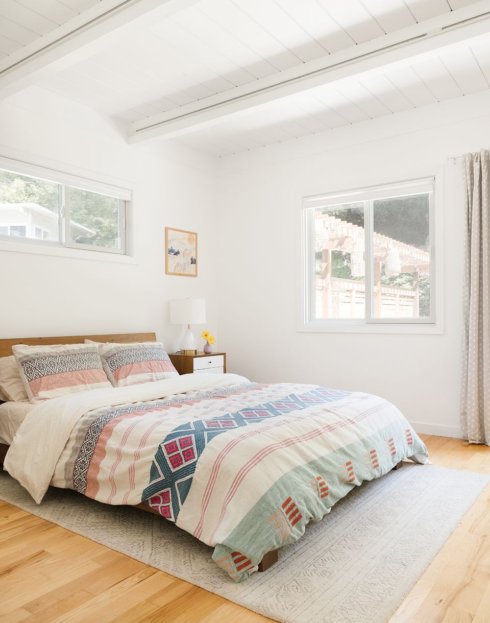 Bright scandinavian bedroom with patchwork bedding, natural wood flooring, and clean white walls