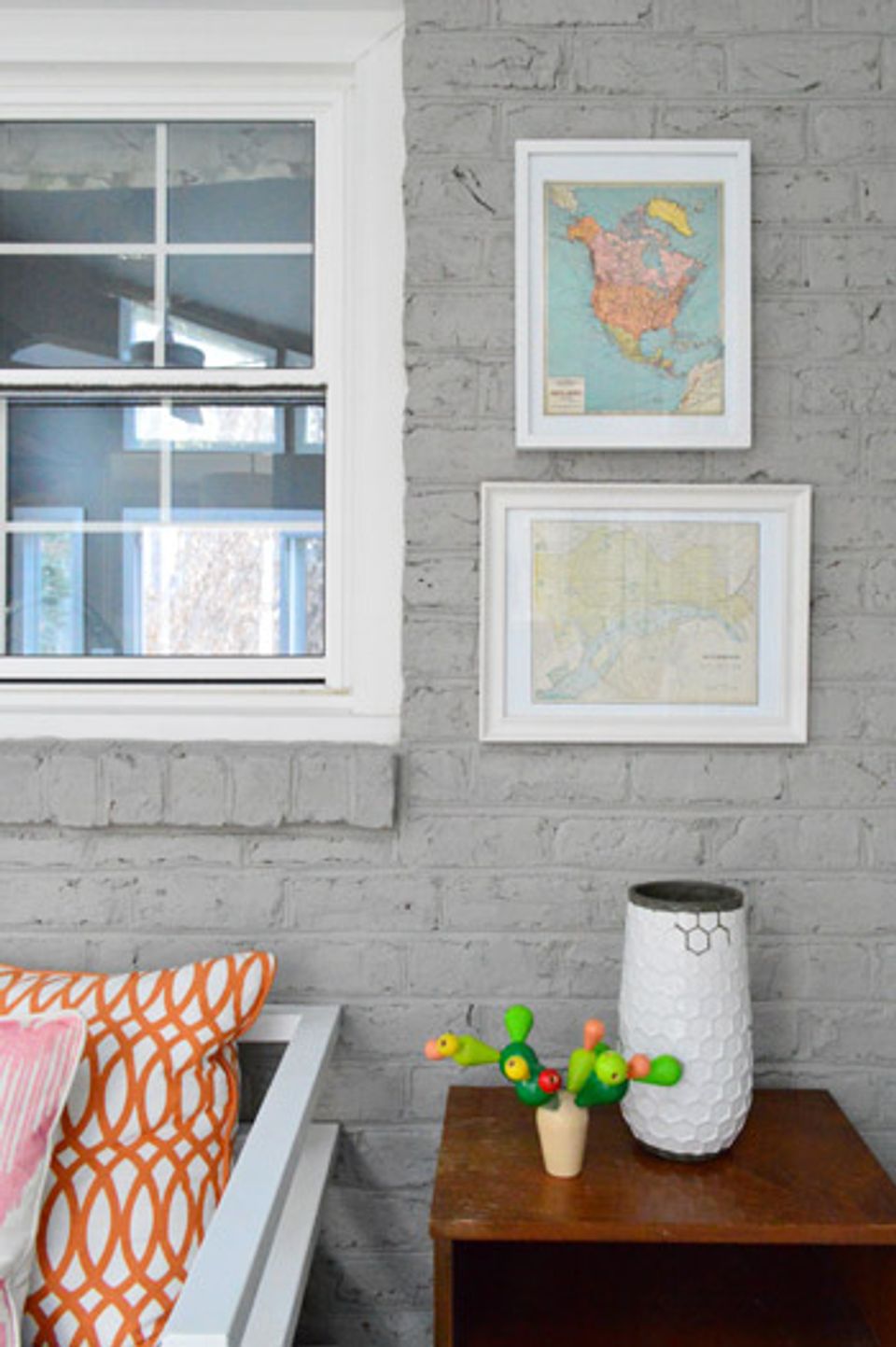 Industrial-modern bedroom corner with vintage maps in white frames on gray brick and colorful geometric pillows