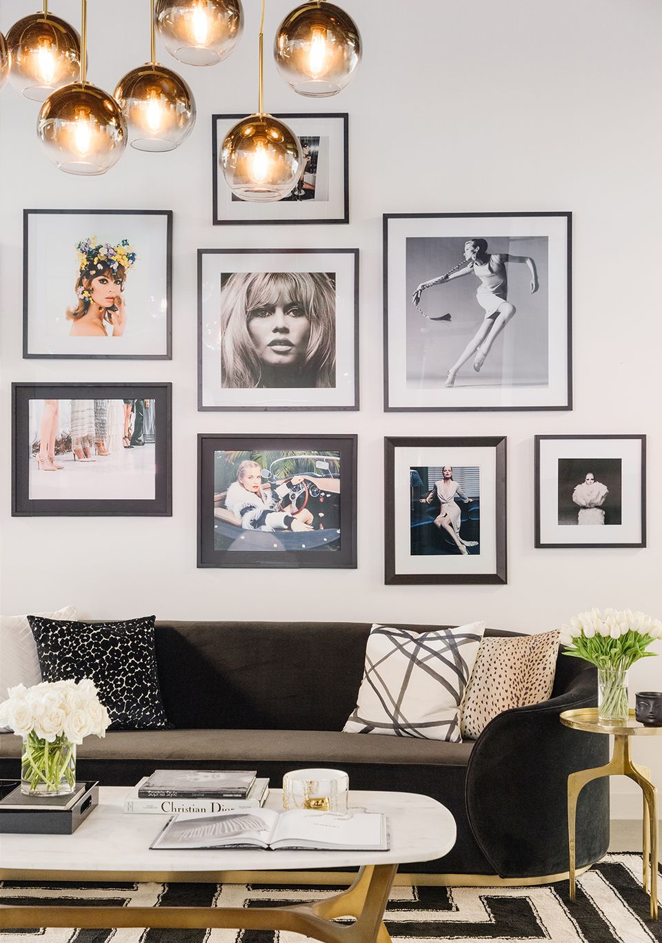 Modern gallery wall with gold pendant lights, black sofa, and monochrome photography frames