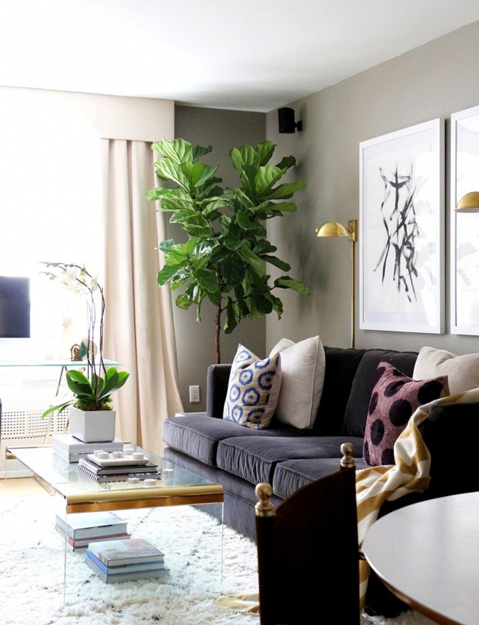 Modern living room with dark sofa, lush greenery, soft neutrals, and gold accents