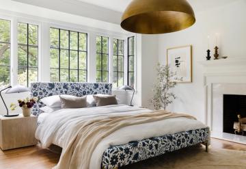 Bright master bedroom with navy floral bedding, brass pendant light, and fireplace under sloped ceiling
