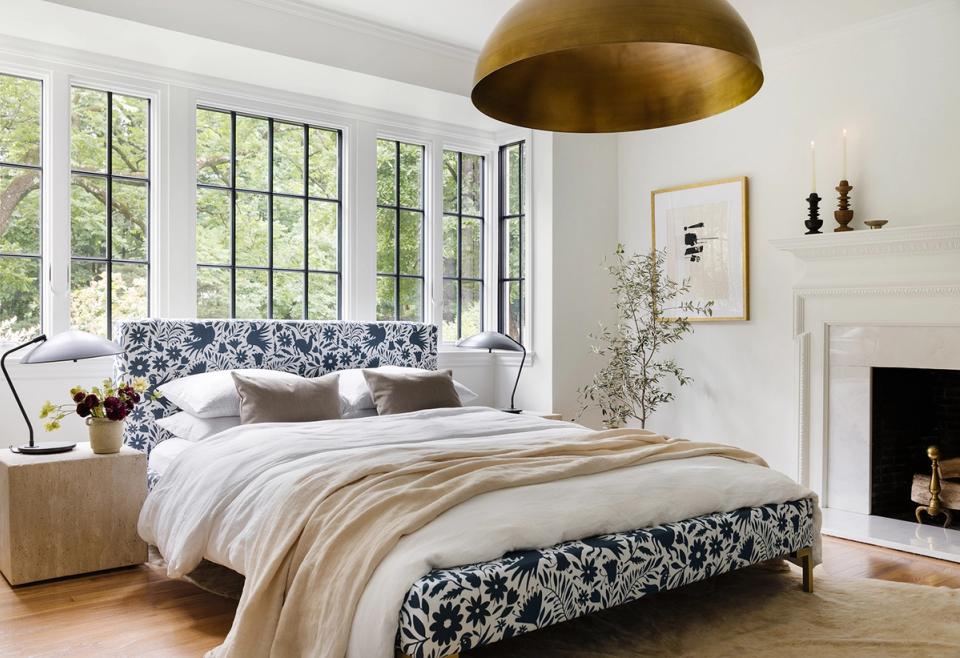 Bright master bedroom with navy floral bedding, brass pendant light, and fireplace under sloped ceiling