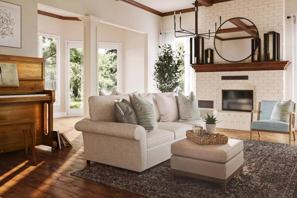 Warm transitional living room with circular bronze mirror, cream sectional, natural light, and wood-beamed ceiling with fireplace