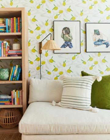 Cozy reading nook featuring lemon wallpaper, cream upholstered seating, olive accents, and open wooden bookshelf