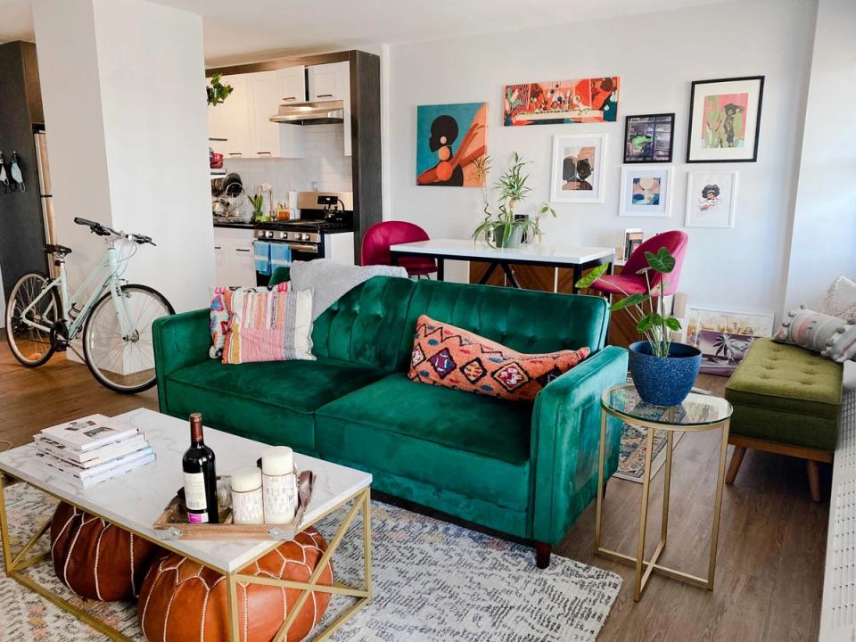Eclectic living room with emerald velvet sofa, vibrant gallery wall, colorful poufs, and warm wood accents creating a personalized, artistic rental space.
