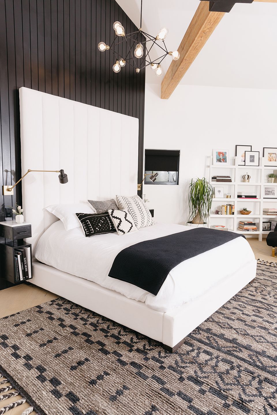 Modern industrial bedroom with black accent wall, white bed, exposed wood beam, and pendant lighting